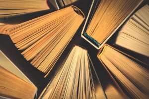A top-down view of several books with their pages fanned out, creating a radial pattern. The yellowed pages suggest they are aged or well-read, while the spines display a variety of colors and textures.