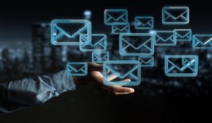 A hand extends from the left side of the image, surrounded by various floating email icons. The background is blurred, depicting a cityscape at night with glowing lights. The visual elegantly represents email communication and networking in the digital age.