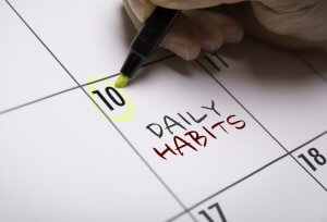 Close-up of a hand marking a calendar date with a green highlighter. The word "HABIT TRACKER" is written in red on the 10th of the month.