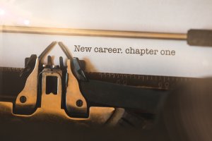 Close-up of a vintage typewriter with a sheet of paper inserted, typed with: "New career. chapter one." Sunlight beams softly illuminate the scene, casting a warm glow over the typewriter keys and paper, symbolizing the start of a fresh career experience.