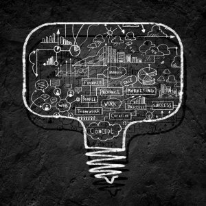 Light bulb-shaped chalk drawing on a blackboard filled with words and sketches related to business concepts. Words include "finance," "marketing," "product," and "teamwork," surrounded by various charts, graphs, and cloud doodles, symbolizing brainstorming ideas often used by billionaires.