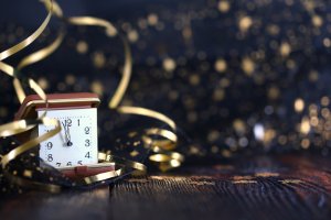 An alarm clock shows midnight, surrounded by gold ribbons and sparkles, set against a dark, festive background. The clock, with its red casing, stands on a rustic wooden surface, symbolizing the celebration of New Year's Eve—an apt metaphor for timely information governance.