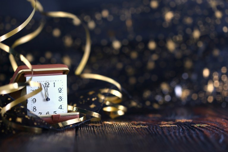 An alarm clock shows midnight, surrounded by gold ribbons and sparkles, set against a dark, festive background. The clock, with its red casing, stands on a rustic wooden surface, symbolizing the celebration of New Year's Eve—an apt metaphor for timely information governance.
