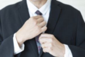 A blurred image of a person wearing a dark suit and adjusting their tie, seemingly preparing for an important job! Their hands are prominently featured, one holding the tie knot and the other adjusting it. The background is out of focus.