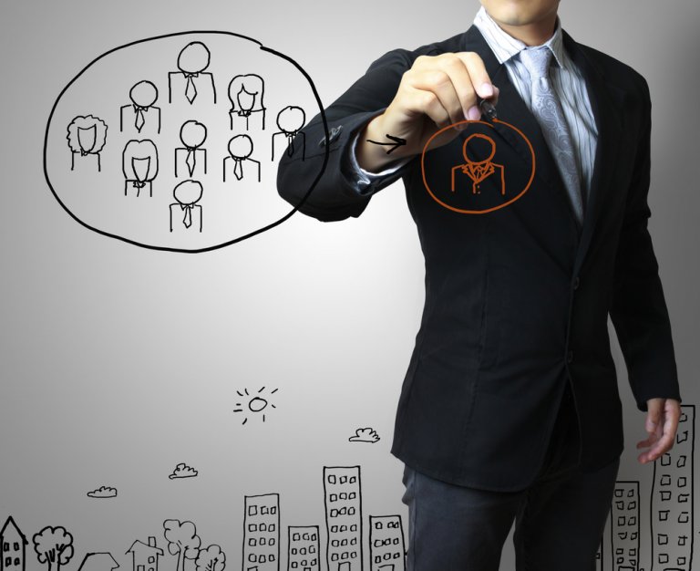 A man in a suit stands pointing at a transparent board. The board displays a diagram of a hierarchical office structure with stick figures representing people, highlighting dynamics in the job market. Below, sketches of buildings and trees create a simple cityscape. The image suggests organizational structure.