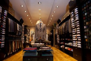 A well-lit men's clothing store with a mannequin dressed in a suit at the center. Shelves and racks on both sides display a variety of shirts, jackets, and pants designed for keeping cool. A table in the foreground holds folded clothes. The store has wooden floors and modern decor.