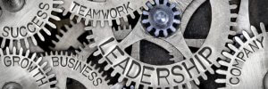 Close-up image of interlocking metal cogs, each one labeled with words like "Leadership," "Teamwork," "Success," "Business," "Growth," and "Company." The arrangement symbolizes the interconnectedness of leadership and these other concepts in achieving organizational goals.