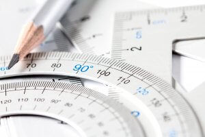 A close-up image of silver protractors and a pencil. The protractors, with clear markings of degrees, especially highlighting the 90-degree angle, showcase precision and perfection. The pencil, with a sharpened tip, lies on top of the protractors.