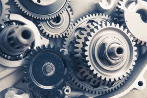 Close-up of interlocking metal gears in a mechanical device, showcasing various sizes and configurations. The cogs have a polished, metallic finish with intricate details, illustrating the perfection and complexity of the machinery.