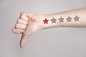 A person extends their arm with a thumbs-down gesture. On the forearm, there is a tattoo of a five-star rating with one star filled in red and the other four stars empty—a subtle critique of good managers. The background is plain white.