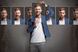 A man in a blue blazer and white t-shirt holds a picture frame over his face, revealing a smiling expression. Behind him are several frames showing different emotional reasoning aspects like happiness, anger, seriousness, and amusement, all set against a gray background.