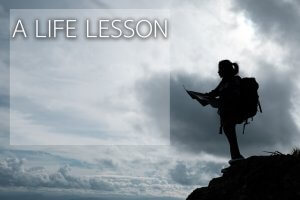 A silhouette of a hiker standing on a rocky edge, holding a map with resolve against a backdrop of a cloudy sky. Text in the image reads, "A LIFE LESSON.