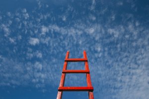 A bright red ladder extends upward against a backdrop of a vibrant blue sky dotted with scattered white clouds. The ladder appears to be reaching towards the sky, conveying a sense of ambition, much like the pursuit of new jobs.