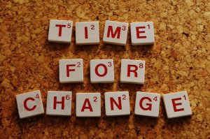 Scrabble tiles spell out "TIME FOR CHANGE" on a corkboard background, serving as the perfect template for inspiration. The letters are in red, each featuring the classic point value found in the game of Scrabble.