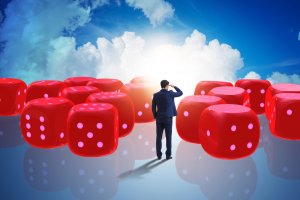 A businessman in a suit stands on reflective ground, surrounded by large red dice with white dots. He faces away, looking towards a glowing horizon against a blue sky with white clouds. The scene mirrors the uncertainty and decision-making involved in debunking resume myths.