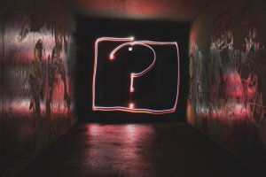 A dark tunnel with colorful graffiti on the walls is illuminated by a large, glowing question mark drawn with light trails at the center. The scene is mysterious and atmospheric, as if questioning resume myths that often lead us through uncertain paths.