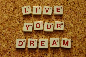 Alphabet tiles arranged on a corkboard spell out "LIVE YOUR DREAM," inspiring your development plan. The background is a textured surface made of small cork pieces, and the tiles feature letters and numbers reminiscent of Scrabble game pieces.