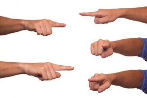 Several hands and fingers, resembling the collaborative effort of teams, are pointing in different directions against a white background. The hands are positioned with various orientations, including fingers pointing left, right, and straight ahead. Some hands have their fingers curled or in a fist.