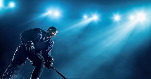 A hockey player in full gear, including a helmet and stick, is skating on an ice rink. Bright stadium lights illuminate the scene, creating a dramatic effect with a blue background. The player appears focused and determined, skating towards success.