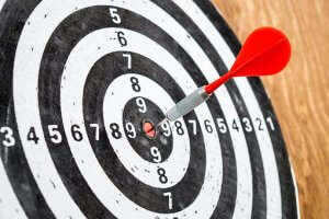 A black and white dartboard with numbers from 1 to 10 is mounted on a wall. A red dart, like hitting the bullseye in an interview, is precisely stuck in the center. The background is blurred, highlighting the accuracy of the throw.