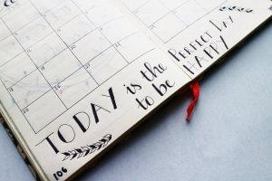 An open planner lies on a flat surface, displaying a month-view calendar on the left page. The right page contains handwritten inspirational text, "Today is the perfect day to be happy," embellished with decorative leaves—a gentle reminder during your job search journey.