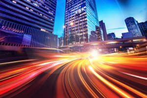 A vibrant cityscape at night featuring tall skyscrapers, much like the meticulous crafting of a cover letter. The image showcases light streaks from fast-moving vehicles on a road, creating dynamic lines of red, yellow, and white light against the bright lights of the city buildings.