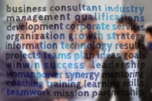 A blurred image of business professionals in suits interacting, overlaid with various business-related terms like "consultant," "cover letter," "strategy," "success," "leadership," and "teamwork" in different shades of blue and black.