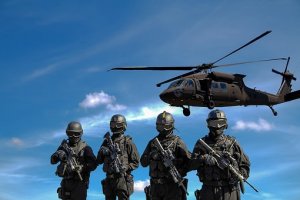 Four heavily armed soldiers clad in black tactical gear stand in a row under a blue sky, showcasing the strong relationships and coordination among them. A black military helicopter hovers above, emphasizing their readiness.