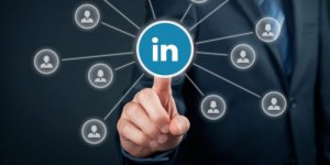 A person in a suit points at a LinkedIn logo surrounded by connected user icons. The image illustrates networking and professional connections, with a blue background highlighting the central LinkedIn symbol and underscoring its significance in the business world.