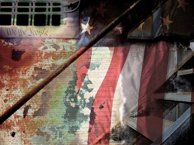 An abstract image blends the US Constitution's "We the People" text, an American flag, and weathered, rusted metal beams. The composition appears layered, with elements of decay and symbols of independence and patriotism intersecting.