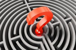A 3D labyrinth with grey walls and pathways has a large red question mark at its center, symbolizing confusion or the search for answers within a complex problem, starting in the middle.
