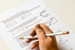 A person's hand holding a pencil is hovering over a sheet of paper filled with mathematical equations and diagrams, including a triangle and a horseshoe magnet. The image suggests the person is working on solving math problems, possibly within the context of special education.