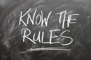 A chalkboard with the words "Know the Rules" written in large, bold, white chalk letters. The background is smudged with chalk dust, marking the path to understanding.