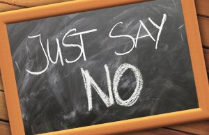 A chalkboard framed in wood displays the phrase "JUST SAY NO" written in large white chalk letters. The board, faintly ghosting from past messages, is set against a background of horizontal wooden planks.