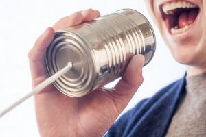 A person holds a tin can with a string attached, speaking into it. Their mouth is open as if they are talking or shouting into the can, creating a playful makeshift communication device often used in children's games—a clever way to avoid ghosting during pretend play.