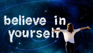 A person with outstretched arms looks up at a night sky with swirling stars and galaxies. The words "believe in yourself" are written in cloud-like letters, capturing the powerful presence of the universe.