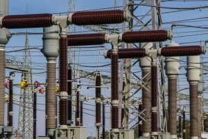 Image shows an electrical substation with multiple large, cylindrical insulators, switches, and cables. The structures are interconnected, and various metal frameworks are visible. A civil engineer's expertise is evident in the setup. The sky is clear and blue in the background, highlighting the intricate design.