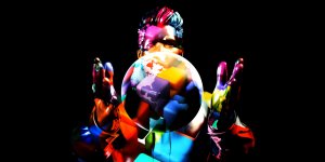 A vibrant, multicolored digital illustration shows a person enveloped in abstract, colorful shapes, standing against a black background with their hands around a globe. The globe prominently displays parts of the Americas at its center, symbolizing the global impact of their job.