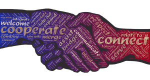 Image of two hands shaking, created using words related to teamwork and collaboration. Words like "cooperate," "connect," "welcome," "job," and "respect" are prominently featured, along with other terms that emphasize unity and partnership. The words are colored in purple and red.