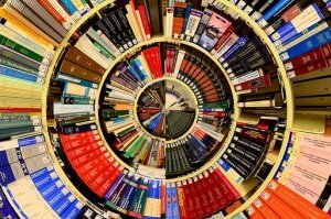 A distorted, spiral image of a bookshelf filled with various colorful books. The perspective twists inward, much like a rolodex in motion, creating a visual effect as if the books are arranged in a vortex, with titles and colors blending together in a circular pattern.