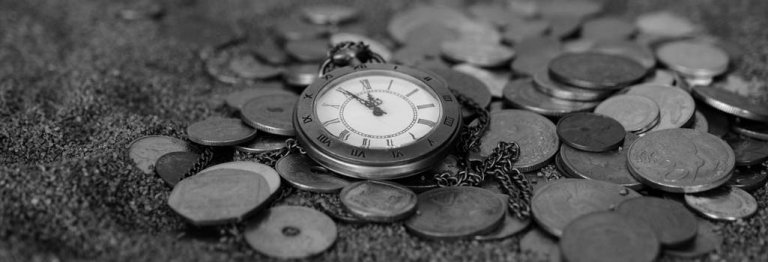 A black-and-white image of an antique pocket watch with Roman numerals on its face lies amidst a scattered collection of coins. The scene evokes a sense of timelessness and history, with the watch slightly worn and the coins varying in design and size, each piece whispering tales of time gone by.