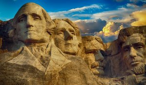 Mount Rushmore National Memorial, featuring the carved faces of four U.S. presidents, stands as a testament to government leadership. The sculptures are embedded in a cliff beneath a partly cloudy sky at sunset, highlighting their detailed expressions.