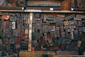 A close-up image of an organized display of various vintage, wooden printing blocks. The blocks include different letters, numbers, and symbols arranged in a visually appealing pattern. The worn and aged appearance of the blocks adds a rustic charm reminiscent of human resources' meticulous documentation over time.