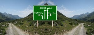 A green road sign in the mountains shows three arrows labeled "Right Way." One arrow points left, one points straight, and one points right. The sign is situated on a dirt trail that splits into three paths, like choices at a busy intersection of meetings amidst lush greenery and mountains.
