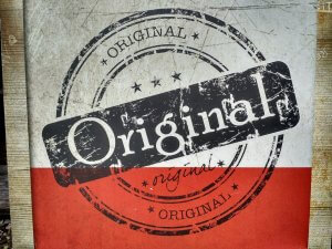 The image displays a textured background with a stamp-like design encasing the word "Original" in large, bold letters. The word is repeated in different sizes and styles, giving a vintage, worn look. The colors used are predominantly black, white, and red, creating an SEO-friendly visual appeal.