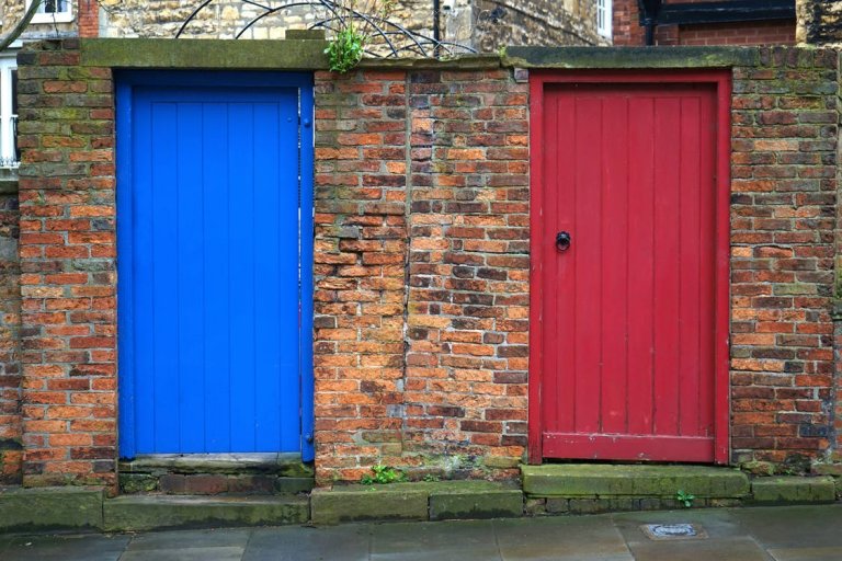 A photograph shows two adjacent doors set in a brick wall, symbolizing employee engagement. The door on the left is painted bright blue, while the door on the right is painted deep red. Both doors have visible wooden planks and are bordered by a slightly weathered stone threshold.