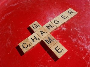 Scrabble tiles arranged to form a cross on a red surface. The vertical word reads "CHANGER" and the horizontal word, sharing the "G" with "CHANGER," reads "GAME." These words perfectly illustrate a game-changer.