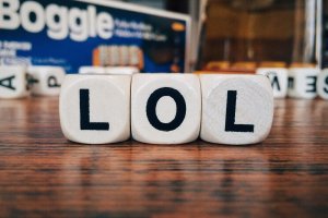 Three white Boggle cubes with the letters "L", "O", and "L" spelling "LOL" are lined up on a wooden surface, capturing a moment of playful serendipity. In the background, the blurry Boggle game box nods to simpler times before social media took over.