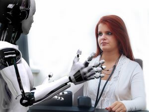 A robot with a sleek, metallic body, powered by artificial intelligence, gestures towards a woman with long red hair seated at a desk. The woman, wearing a white blouse, looks attentively at the robot. The background is white and minimalistic.