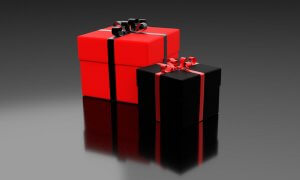 Two wrapped gift boxes with curly ribbon bows are shown against a sleek black gradient background, capturing your attention. The larger box is red with a black ribbon, and the smaller box is black with a red ribbon. The smooth surface they rest on creates a reflection of the boxes.